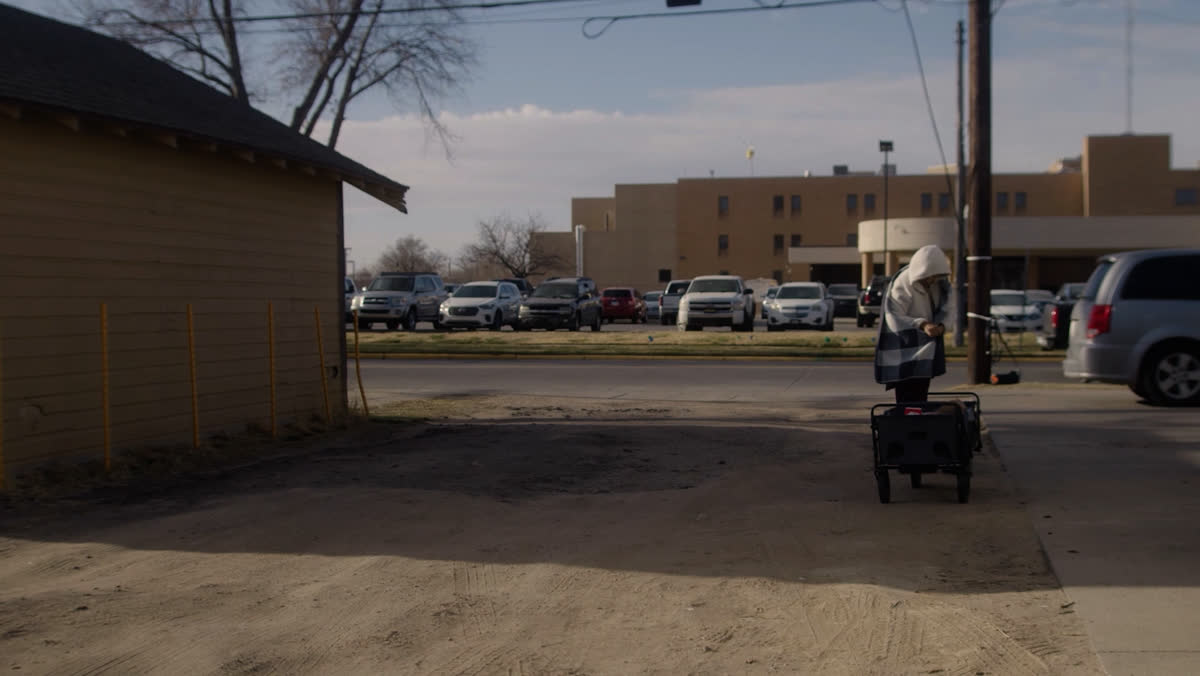 A woman pushes a cart across an empty lot